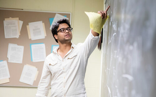 Student in classroom writing on blackboard.
